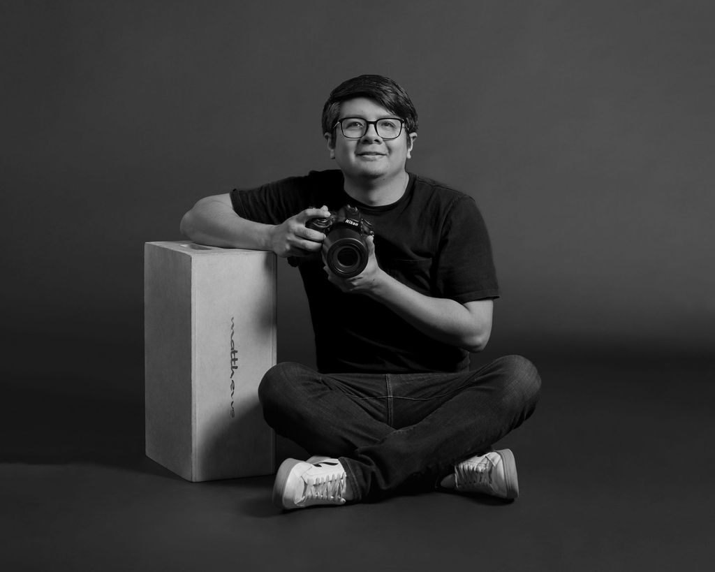 Black & White Photo of photographer sitting with camera in a studio.