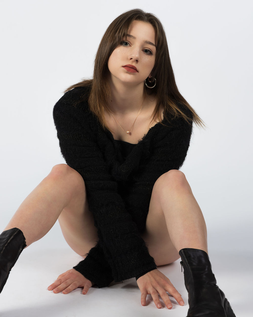 Girl sitting in white studio wearing black bodysuit with long sleeves looking directly into camera.