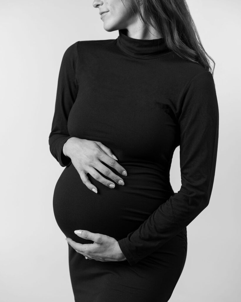 Black and white photo of pregnant mom wearing fitted black dress holding her baby bump.