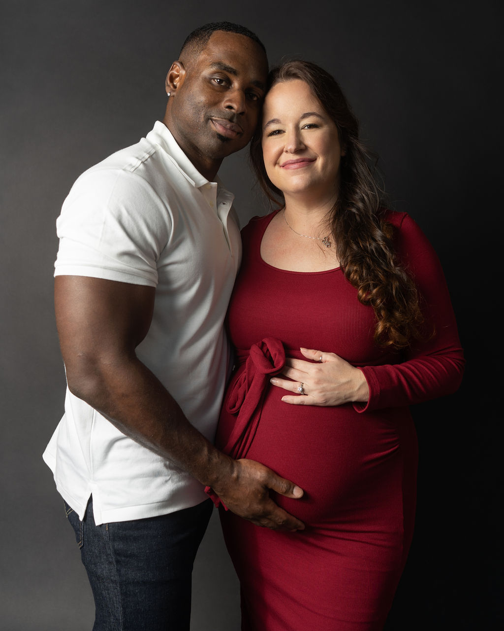 An Austin couple taking maternity photos together standing in a studio while hugging and holding the baby bump.